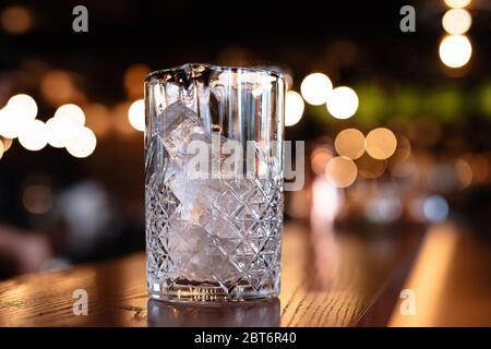 Das kristallklare Glas ist mit Eis gefüllt, das Eis im Glas liegt in Würfeln, eine Theke, ein brauner Tisch, der Hintergrund ist verschwommen und in li Stockfoto