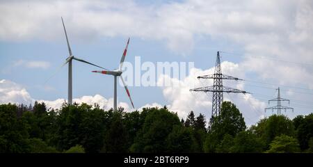 Zwei Windturbinen hinter einem Waldgebiet und ein Strommast daneben Stockfoto
