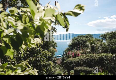 Person, die sich auf einer schwimmenden Plattform aus Holz auf dem Kratersee der Laguna de Apoyo, Nicaragua, durch Bäume gesehen, entspannt Stockfoto