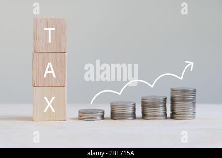 Der Buchstabe "STEUER" auf einem hölzernen Würfel und Münzen sind in einem Balkendiagramm mit wachsendem Pfeilsymbol angeordnet. Stockfoto