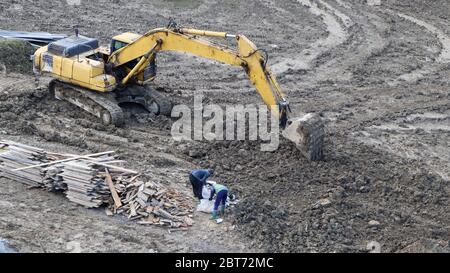 Luftaufnahme eines gelben Arbeitsbaggers auf einer schlecht gepflegten Feldstraße mit Personen, die auf einer Baustelle arbeiten. Bauindustrie Stockfoto