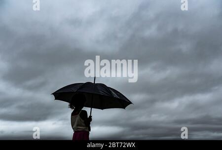 Guwahati, Assam, Indien. Mai 2020. Ein Mädchen unter einem Schirm am Ufer des Brahmaputra Flusses im Hintergrund von dunklen Wolken, die den Himmel an einem regnerischen Tag in Guwahati bedecken. Kredit: David Talukdar/ZUMA Wire/Alamy Live News Stockfoto