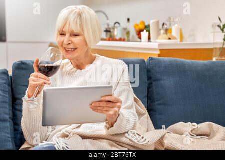 Ältere Frau mit Wein in der Hand mit modernen Tablet-Computer Stockfoto
