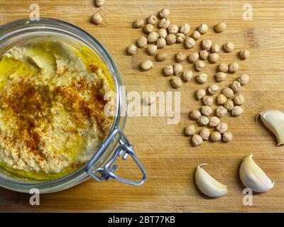 Hausgemachte Hummus im Glas mit Kichererbsen und Knoblauchzehen auf Holz Hintergrund Stockfoto