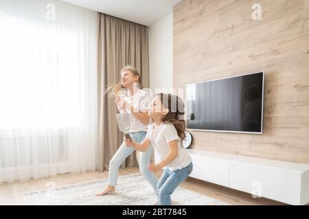 Zwei Schwestern, die Spaß haben, im Wohnzimmer zu tanzen und Karaoke zu singen, Happy Family Concept Stockfoto