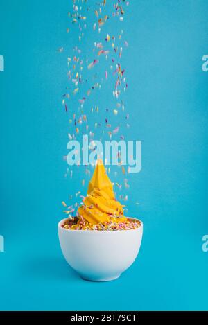 Schüssel Eis mit fallenden Streuseln auf blauem Hintergrund Stockfoto