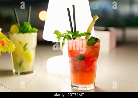 Zwei Kristallgläser mit roten und gelben Cocktails auf einem Tisch mit einer Lampe in der Nacht Stockfoto