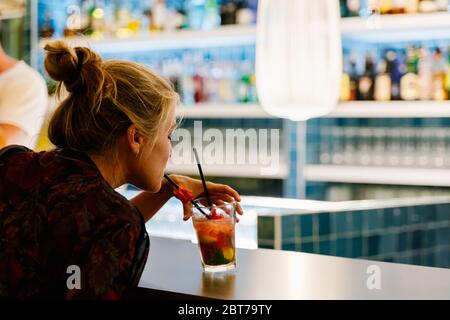 Blonde Frau auf dem Rücken trinkt einen Cocktail mit Stroh in einer Bar in einem Nachtclub Stockfoto