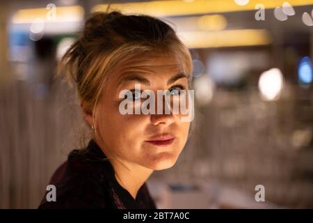 Detail des Gesichts einer blonden Frau mit gedrehtem Kopf zur Kamera in einem Innenraum mit reflektierten Lichtern in der Nacht Stockfoto