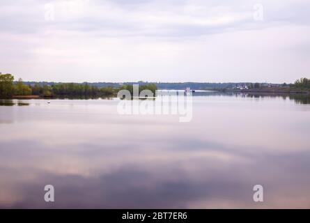 Russische Landschaft, Wolga Fluss in der Morgendämmerung in hellen Dunst. Rosa-lila Wolken spiegeln sich in ruhigem Wasser. Frachtschiff geht stromaufwärts der Volg Stockfoto