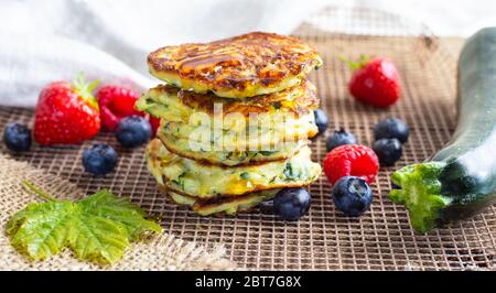 Frische Stapel von köstlichen hausgemachten Zucchini Pfannkuchen mit Honig Ahornsirup, Sommerfrüchte, Zucchini und Ahornblatt auf Küchengrill gekrönt. Nahaufnahme. Rezept, Kochen, Saison, Menükonzept Stockfoto