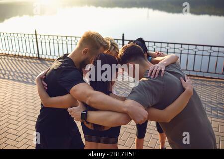 Eine Gruppe junger Menschen in Sportbekleidung legte sich die Hände zusammen, während sie morgens im Morgengrauen in einem Park standen. Ein Team von Sportlern trainiert zusammen. Stockfoto