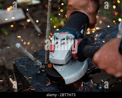 Arbeiter schneidet überschüssige Verstärkung im Fundament mit einem Winkelschleifer, Metall Funken fliegen Stockfoto