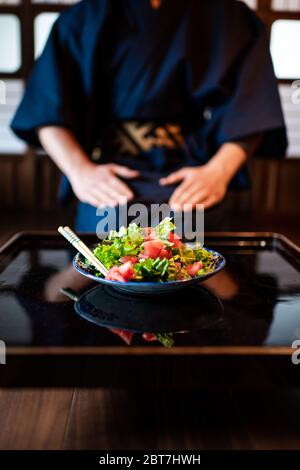 Traditionelles japanisches Zimmer im Ryokan-Restaurant mit schwarz lackiertem Holztisch und Salatgericht mit Mann in Kimono oder Yukata im Hintergrund Stockfoto