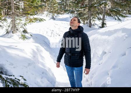 Junger glücklicher Mann auf schneebedeckten Bergwegen in den Dörfern von Okuhida Shinhotaka Ropeway in der Präfektur Gifu, Japan Park, der in Mantel und Jeans aufschaut Stockfoto