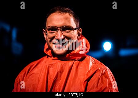 Glücklicher Mann Gesicht Nahaufnahme mit Brille Blick auf Kamera lächelnd in der Nacht in Takayama, Gifu Präfektur in Japan tragen Poncho bei regnerischem Wetter und b Stockfoto