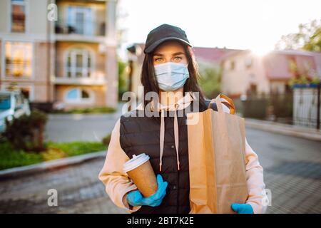 Gesundheitsschutz, Sicherheit und Pandemie Konzept - Lieferung Frau in schützende Gesichtsmaske und Handschuhe mit einer Tasche von Lebensmitteln und Kaffee Stockfoto