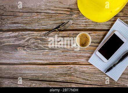 Workspace Builder Architekt Bürotisch Schreibtisch, leer offenes Notebook mit Stift auf gelben Hut mit Tasse Kaffee, Smartphone-Brille auf Holzschreibtisch Stockfoto