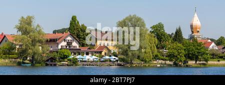 Panorama von Weßling. Fantastische bayerische Landschaft mit Biergarten, Bäumen und einer Kirche (St. Christkönig). Im Vordergrund der Weßling See. Stockfoto