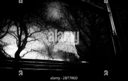 Altmodische Lampe im Fenster des Ghost-Busses, der in Edinburgh während des Lockdown 2020 geparkt wurde, mit Reflexen von Bäumen in den Fenstern. Dramatisches Schwarz-Weiß. Stockfoto