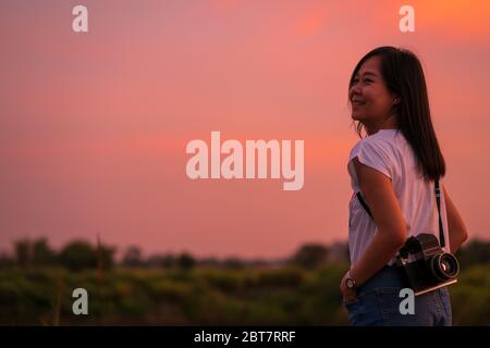 Porträt von schönen lächelnden asiatische Frau mit Mittelformat-Filmkamera mit bunten Sonnenuntergang Himmel Hintergrund Stockfoto