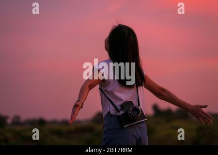 Porträt der schönen Freiheit asiatische Frau mit Mittelformat-Filmkamera mit bunten Sonnenuntergang Himmel Hintergrund halten Stockfoto
