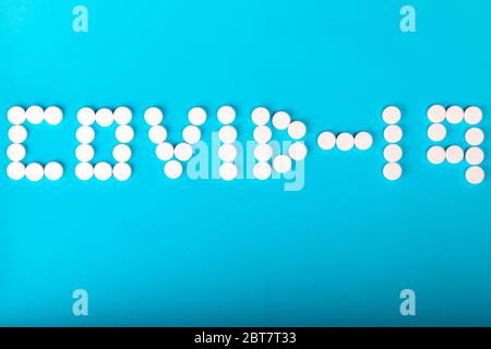 Inschrift COVID-19 aus weißen medizinischen Pillen auf einem cyanfarbenen Papierhintergrund. Idee wartet auf einen Impfstoff. Medizinisches Coronavirus-Konzept. Banner – Ansicht Von Oben. Stockfoto