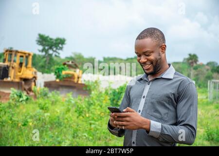 afrikanischer landwirtschaftlicher Geschäftsmann, der ein Mobiltelefon auf einem Grundstück benutzt Stockfoto