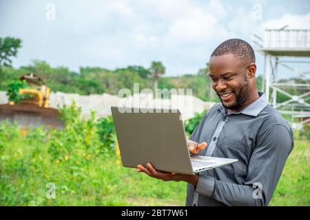 Junger afrikanischer Geschäftsmann, der einen Laptop auf einem Grundstück benutzt Stockfoto