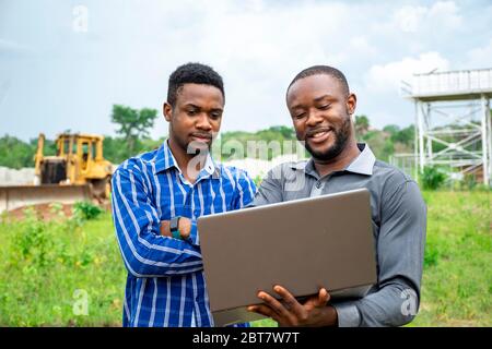 afrikanische landwirtschaftliche Geschäftsleute, diskutieren mit einem Laptop auf einem Stück Land Stockfoto