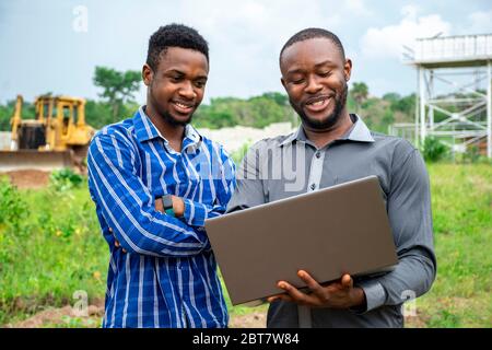 afrikanische landwirtschaftliche Geschäftsleute, diskutieren mit einem Laptop auf einem Stück Land Stockfoto