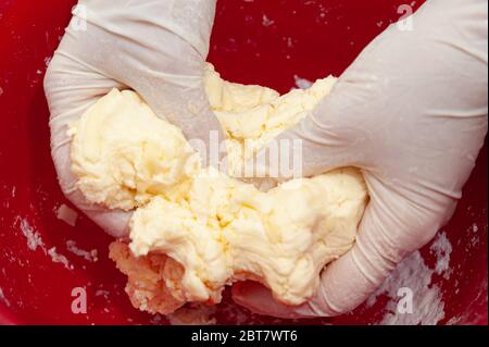 Handschuhhandchen, die den Teig kneten. Herstellung von köstlichen und traditionellen brasilianischen Käsebrot (Pao de Queijo). Nahaufnahme. Horizontale Aufnahme. Stockfoto