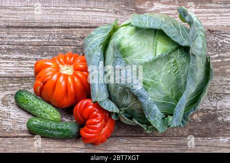 Bio-Gemüse auf einem Holzhintergrund. Kohl, Tomaten und Gurken. Rustikales Stillleben auf den Brettern Stockfoto