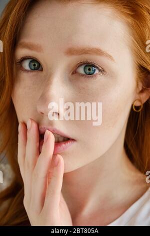 Ein enges Porträt eines schönen rothaarigen Mädchens mit blauen Augen. Schaut in den Rahmen und drückt seine Finger auf seine Lippen Stockfoto