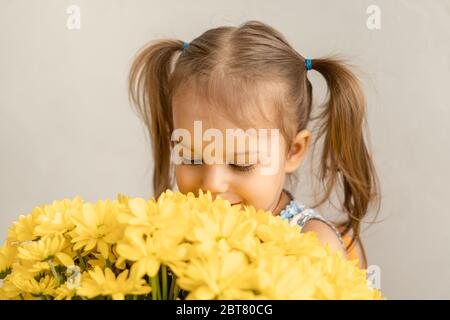 Kindheit, Feiertage, Blumen, Geschenke Konzept - kleine süße drei-jährige Mädchen mit zwei Pferdeschwänzen auf dem Kopf in blau bunten Kleid hält groß Stockfoto