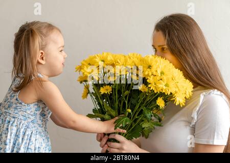 Mutterschaft, Muttertag, Geburtstag, Kindheit, Familienkonzept - close-up kleines Mädchen in blau bunten Kleid gratulieren und geben junge Mutter hell Stockfoto