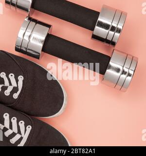 Kleine Metallhanteln und Sneaker zum Training auf rosa Hintergrund. Stockfoto