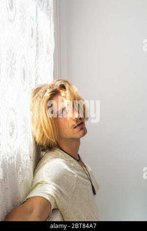 Junger Mann mit mittellangen blonden Haaren frustriert, nicht in der Lage, das Haus zu verlassen. Blick auf die Kamera auf weißem Hintergrund. Einsamkeit und ti Stockfoto