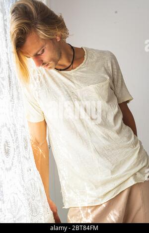 Junger Mann mit mittellangen blonden Haaren frustriert, nicht in der Lage, das Haus zu verlassen. Blick auf einen weißen Hintergrund. Einsamkeit und Stille Konzept. Stockfoto