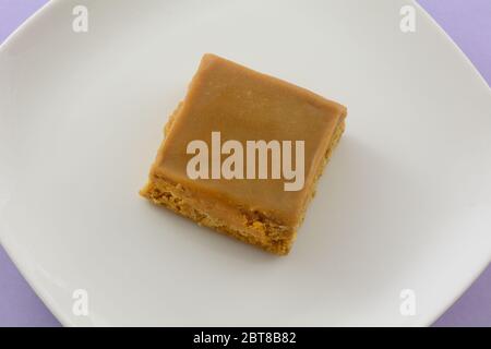 Toffee Flapjack quadratische Kuchenleiste auf weißem Teller auf Lavendelhintergrund Stockfoto