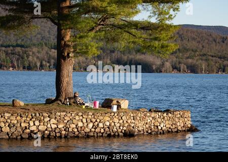 Ein eineinleiner Fischer, der sich an einem Baum am Osborne Point am Lake Pleasant in den Adirondack Mountains, NY, USA, lehnt Stockfoto