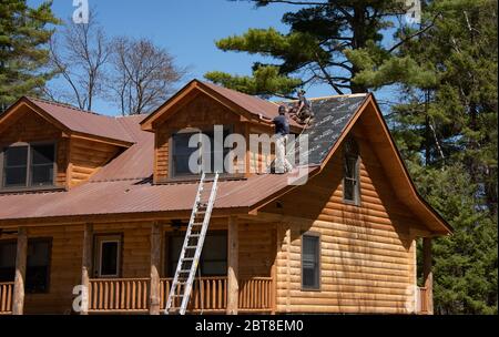 Zwei Bauarbeiter installieren ein Metalldach auf einer neu gebauten Blockhütte in den Adirondack Mountains, NY USA Stockfoto