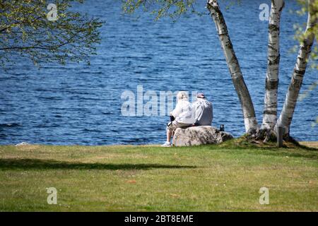 Zwei Senioren sitzen auf einem Felsen, entspannen im Park am Lake Pleasant, NY USA in den Adirondack Mountains. Stockfoto