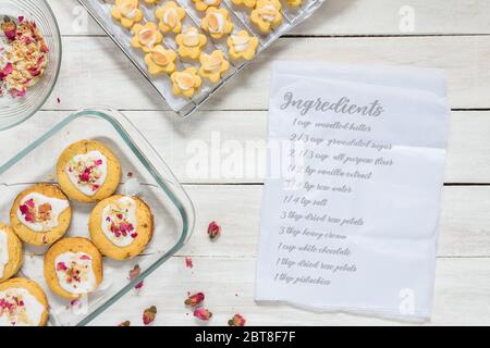 Hausgemachte Rose kurze Brot Cookies auf weißen Holztisch mit Papier und Zutaten Liste - Lebensmittel und Lifestyle-Bild. Stockfoto