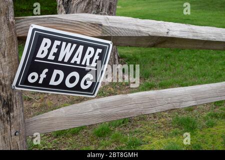 Vorderer Rasen mit Baum und zwei Schienen Holzzaun mit Schild, das "Vorsicht Hund" liest Stockfoto