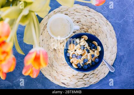 Morgens, Frühstück, Müsli Mini Pancake Müsli, Mini Pfannkuchen in einer dunkelblauen Schüssel mit Ahornsirup Honig mit Heidelbeere und und und eine Tasse Kaffee. St Stockfoto