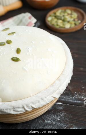 Frisch gekochter Hefeteig in einem Korb zum Backen mit Kürbiskernen für die Herstellung von frischen Naturkuchen und Brot ein dunkler Holzhintergrund, Kopie Stockfoto