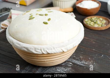 Frisch gekochter Hefeteig in einem Korb zum Backen mit Kürbiskernen für die Herstellung von frischen Naturkuchen und Brot ein dunkler Holzhintergrund, Kopie Stockfoto