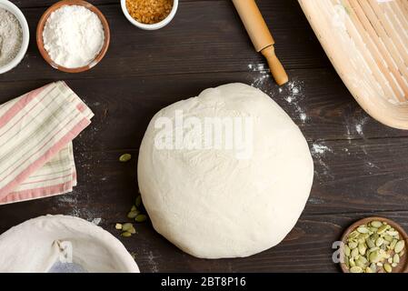 Frisch zubereitetes Laib selbstgemachten weißen gesunden Brot mit Kürbiskern in einem Teigkorb ist bereit zum Backen auf einem dunklen Holzhintergrund, Kopierraum. Stockfoto