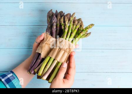 Bunche von hausgemachten frischen Bio-grünen und lila Spargel in einer Frau die Hände zum Kochen vegetarische gesunde Lebensmittel auf einem blauen Holzhintergrund, Kopie Stockfoto